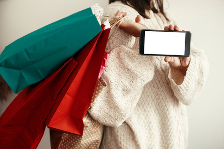 Black Friday. Christmas Sales. Happy Girl holding phone with empty screen and carrying colorful...