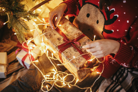 girl hands opening Christmas gift box on at golden beautiful christmas tree with lights in festive room. winter holiday atmospheric moments. seasons greetings. Merry Christmasの写真素材