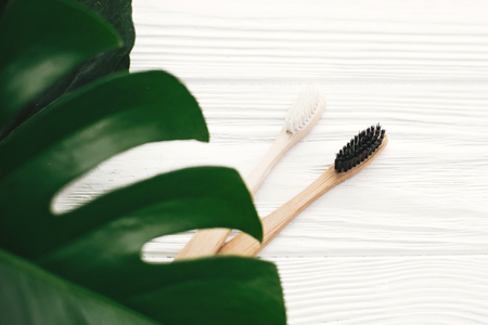 Zero waste concept. Natural eco friendly bamboo toothbrushes on white wood with green monstera leaves. Eco products plastic free. Hygiene care and treatmentの写真素材