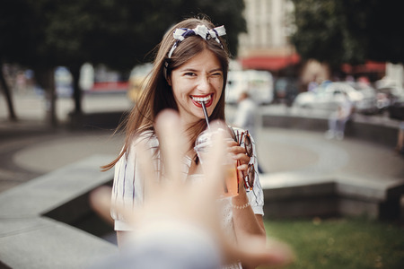 Beautiful stylish young woman holding drink and relaxing in city street. Happy hipster girl in retro...
