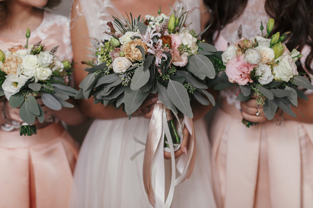 Bridesmaids and bride holding modern wedding bouquets of pink roses and green eucalyptus with pink ribbons. Stylish Contemporary bouquets on soft fabric. Wedding arrangementsの写真素材