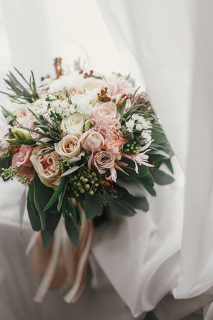 Stylish wedding bouquet of pink roses and green eucalyptus on background of window. Modern bride's bouquet on soft fabric in morning light. Wedding arrangements and decorの写真素材