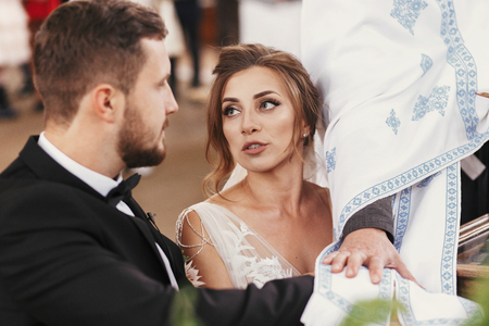 Bride and groom making oaths  and priest holding their hands on holy Bible. Wedding matrimony in church. Exchanging vows. Emotional romantic momentsの写真素材