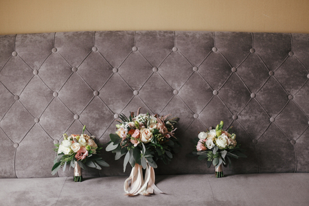 Modern wedding bouquets of pink roses and green eucalyptus with pink ribbons on stylish grey sofa. Contemporary composition of bridesmaids and bride bouquets on soft fabricの写真素材