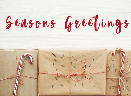 Season's greetings text on christmas stylish presents with red ribbon, candy cane, pine branches and cones. Happy Holidays card. Merry Christmas and Happy New Yearの写真素材