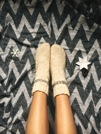 Stylish christmas woolen socks on woman legs, relaxing on plaid with holiday ornaments in festive...