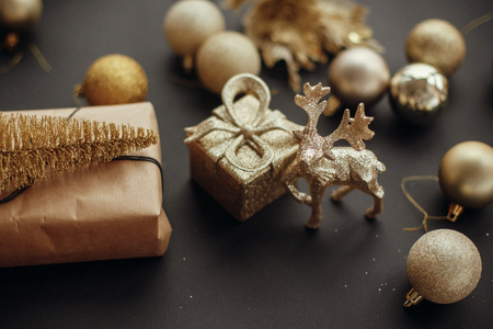 Merry Christmas and Happy New Year. Christmas gold tree, gift box, reindeer and glitter baubles on stylish black background. Modern Christmas  image. Seasons greetings card.の写真素材