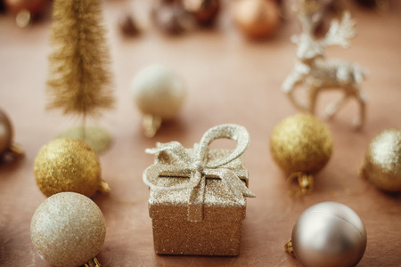 Christmas golden gift box on background of glitter tree and reindeer, shiny baubles and balls on rustic background. Modern gold decorations and present. Seasons greetings. Merry Christmasの写真素材