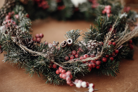 Details of rustic Christmas wreath, cinnamon and berries closeup. Fir branches with red berries,pine cones,ribbon, cotton on rustic wood. Atmospheric moody image at holiday workshopの写真素材