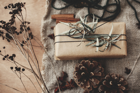 Merry Christmas concept, rustic atmospheric flat lay. Stylish gift box with green branch and fir branches, anise, pine cones, cinnamon on rustic wooden background. Simple eco wrapped presentの写真素材