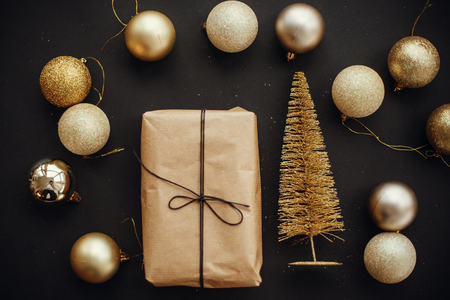 Christmas gold tree and  gift box with glitter baubles on stylish black background. Modern Christmas flat lay image. Seasons greetings card. Merry Christmas and Happy New Yearの写真素材