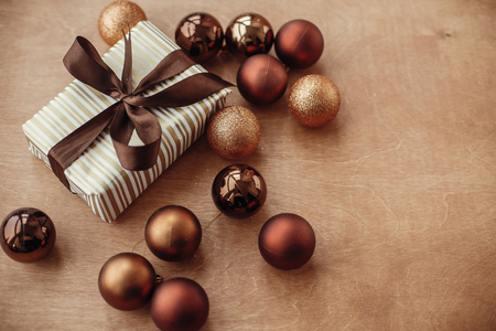 Christmas stylish gift box with glitter ornaments and baubles on rustic wooden background. Modern brown and gold decorations. Seasons greetings. Merry Christmasの写真素材