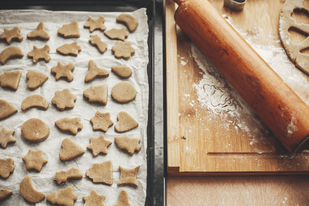 Christmas raw gingerbread cookies on baking tray and wooden rolling pin on rustic wooden table. Tree, stars, jingle bells, gingerbread man cookies.  Atmospheric stylish imageの写真素材
