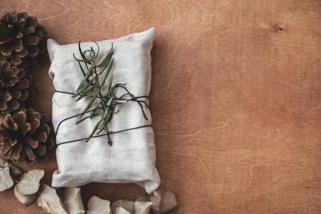 Stylish christmas rustic gift wrapped in linen fabric with green branch on wooden table with pine...