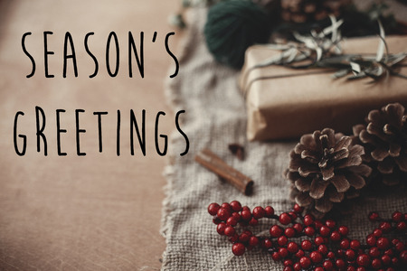 Season's greetings text sign on stylish rustic christmas gift box with fir branches, red berries, pine cones, cinnamon on rustic wood. Atmospheric image. Seasonal greeting cardの写真素材