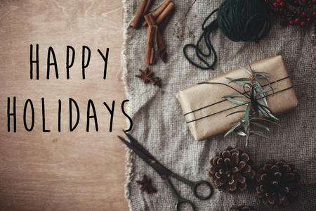 Happy Holidays text sign on stylish rustic gift box with green branches, anise, pine cones, cinnamon on rustic wood. Seasonal greeting card. Simple eco present. Atmospheric imageの写真素材