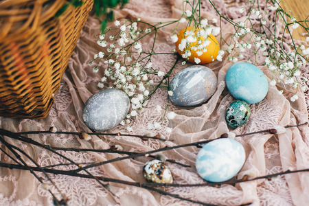 Stylish easter eggs with flowers and branches on cloth at rustic basket on wooden background. Easter hunt concept. Modern easter eggs painted with natural dye. Happy Easterの写真素材