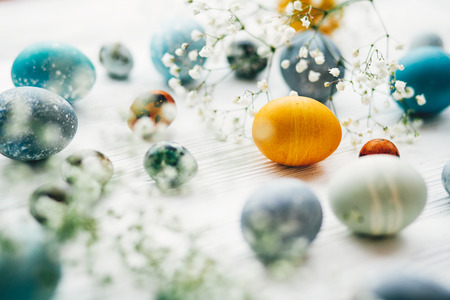 Stylish easter eggs with spring flowers on white wooden background. Modern easter eggs painted with natural dye in blue, grey, yellow marble color. Happy Easter, greeting cardの写真素材