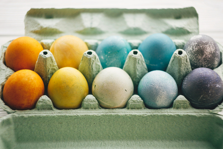 Stylish easter eggs in carton tray on white wooden background. Modern colorful easter eggs painted with natural dye in different colors. Happy Easter, eco conceptの写真素材