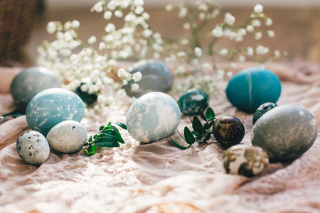 Happy Easter. Stylish easter eggs with spring flowers on rustic fabric on wood in sunny light. Modern easter eggs painted with natural dye in blue, grey marble color. Greeting cardの写真素材