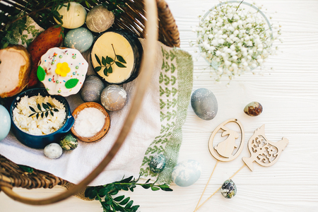 Easter basket with stylish eggs, easter bread, ham, sausage, butter, and flowers, easter wooden bunny and chicken decorations on rustic wood, top view. Happy Easter conceptの写真素材