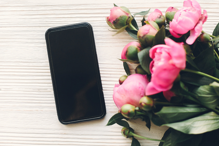 lovely pink peonies and phone with empty screen on rustic white wooden background, top view, space for text. floral greeting card mock-up, flat lay. happy mothers dayの写真素材
