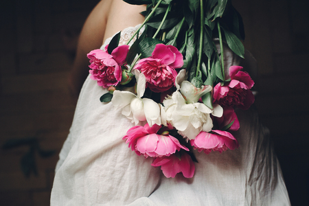 beautiful pink peonies on legs of boho girl in white bohemian dress, top view. space for text. stylish hipster woman sitting with flowers in moody morning. atmospheric sensual momentの写真素材