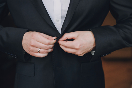 Stylish groom putting on black suit, getting ready in the morning near window in soft light, before wedding ceremony. Rich businessmanの写真素材