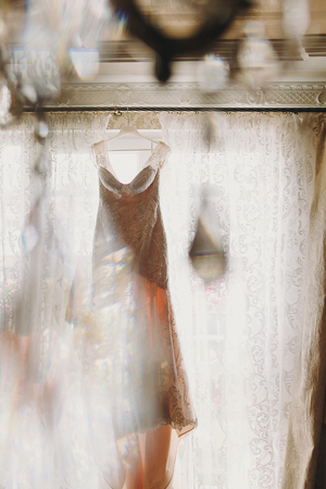 Luxury modern wedding dress hanging at window, creative view through diamond stones. Amazing stylish wedding gownの写真素材