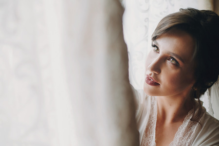 Beautiful stylish brunette bride posing in silk robe near wedding gown in the morning. Sensual portrait of happy woman model  getting ready for wedding dayの写真素材