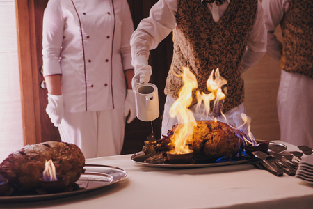 Delicious meat in fire at wedding reception in restaurant. Chef cooking tasty meal with fire show, luxury catering. Smoked meat in flames. Thanksgiving feastの写真素材