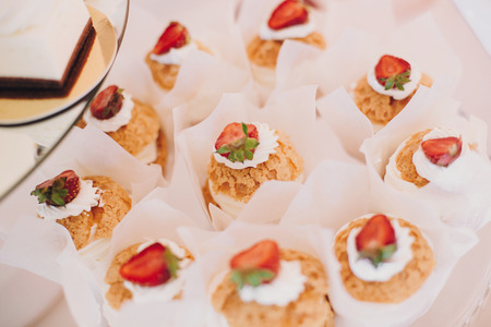 Delicious eclairs cupcakes, desserts and sweets on table party at wedding reception. White and pink...