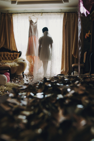 Beautiful stylish brunette bride in silk robe and long veil walking to her amazing wedding dress in the morning. Sensual portrait of happy woman model getting ready for wedding dayの写真素材