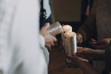 Happy stylish wedding couple holding candles with fire and light them up with candle from parents, family fire tradition at reception. Bride and groom at holy matrimonyの写真素材