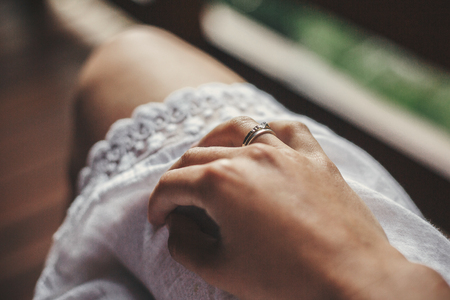 Hand with engagement ring on girl white bohemian dress on wooden porch in summer mountains. Silver ring with crystal. Girl relaxing in woods. Just engageの写真素材