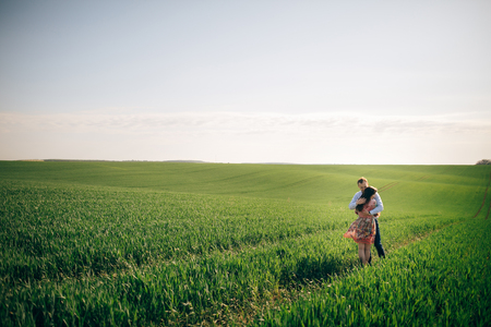 Beautiful young couple gently hugging in sunshine in spring green field. Happy family embracing in green meadow with fresh grass in sunlight. Romantic moments. Valentine day.の写真素材