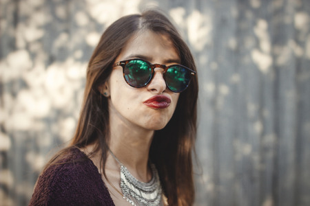 Portrait of happy boho girl in sunglasses having fun and smiling in sunny street. Stylish hipster carefree girl posing on background of wooden wall. Space for text. Summer vacationの写真素材