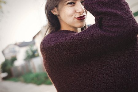 Happy hipster carefree girl in sweater walking in evening summer city. Stylish bohemian girl with funny emotions having fun and relaxing in sunny street. Summer vacation and travelの写真素材
