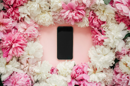 Pink and white peonies and phone with blank screen on pastel pink paper. Stylish flat lay with copy space. Happy mothers day, floral greeting card mockup. International Womens Day.の写真素材