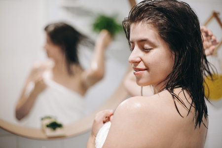 Young happy woman in white towel enjoying spa and wellness, relaxing in bathroom with mirror. Hair and body care. Slim sexy woman with natural skin and wet hair after shower .の写真素材