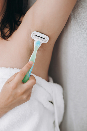 Hand holding plastic razor and shaving hairy armpit. Young woman shaving armpits with plastic razor closeup in home bathroom. Skin care. Hair Removal concept. Copy spaceの写真素材