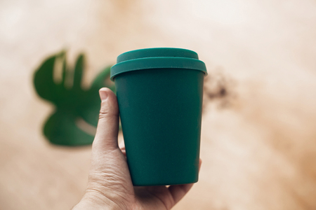 Ban single use plastic. Hand holding eco reusable coffee cup on wooden background. Coffee cup from bamboo fiber, zero waste concept.  Take away coffee in your cup. Sustainable lifestyleの写真素材