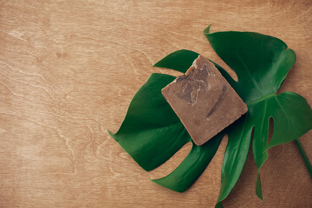 Natural soap on wooden background with green monstera leaf. Plastic free beauty essentials. Zero waste concept, flat lay with copy space. Sustainable lifestyleの写真素材