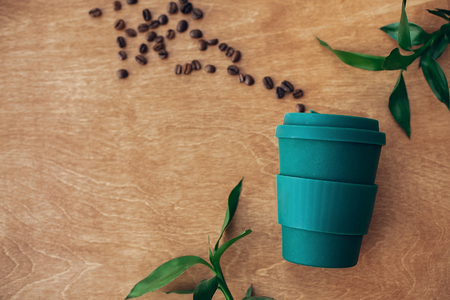 Stylish reusable eco coffee cup  on wooden background with coffee beans and green bamboo leaves. Ban single use plastic. Zero waste concept, flat lay. Sustainable lifestyle. Natural bamboo cupの写真素材