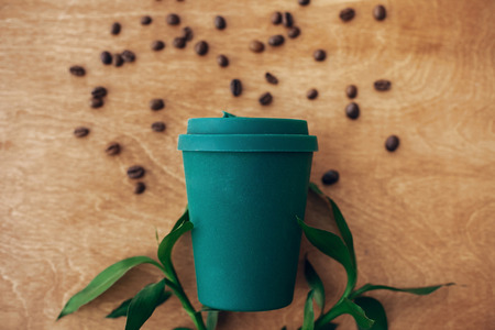 Zero waste concept, flat lay. Stylish reusable eco coffee cup  on wooden background with coffee beans and green bamboo leaves. Ban single use plastic. Sustainable lifestyle. Natural bamboo cupの写真素材