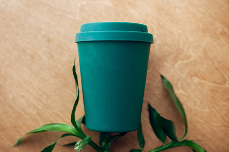 Ban single use plastic. Stylish reusable eco coffee cup and bamboo leaves on wooden background, flat...