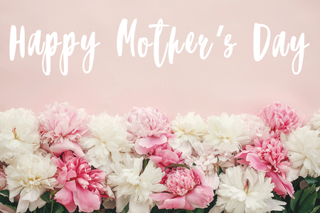 Happy Mother's Day text sign on peonies flat lay. Pink and white peonies border on pastel pink paper with space for text.  Stylish floral greeting card.の写真素材