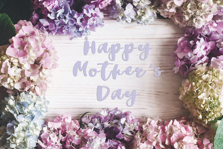 Happy Mother's Day text sign on beautiful hydrangea flowers frame on rustic white wood, flat lay. Colorful pink,blue,green,white border of hydrangea. Stylish floral greeting card.の写真素材