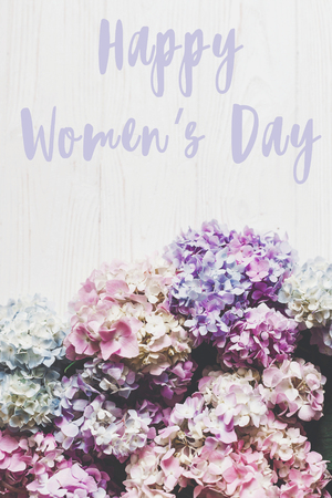Happy Women's Day text sign on beautiful hydrangea flowers on rustic white wood, flat lay. Colorful border of hydrangea. Stylish floral greeting card. International womens day 8 marchの写真素材