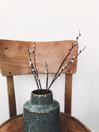 Simple willow buds branches in stylish vase on wooden rustic chair in home. Hello spring concept. Countryside living. Modern rural still life. Easter decorationsの写真素材